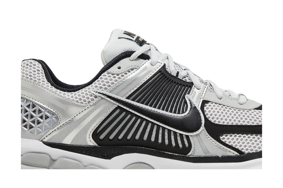 Gros plan de la Nike Zoom Vomero 5 Metallic Silver Black : mesh gris respirant, renforts argentés, Swoosh noir et marquage Zoom sur la semelle